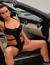 Hot mature brunette dressed in black posing in a car